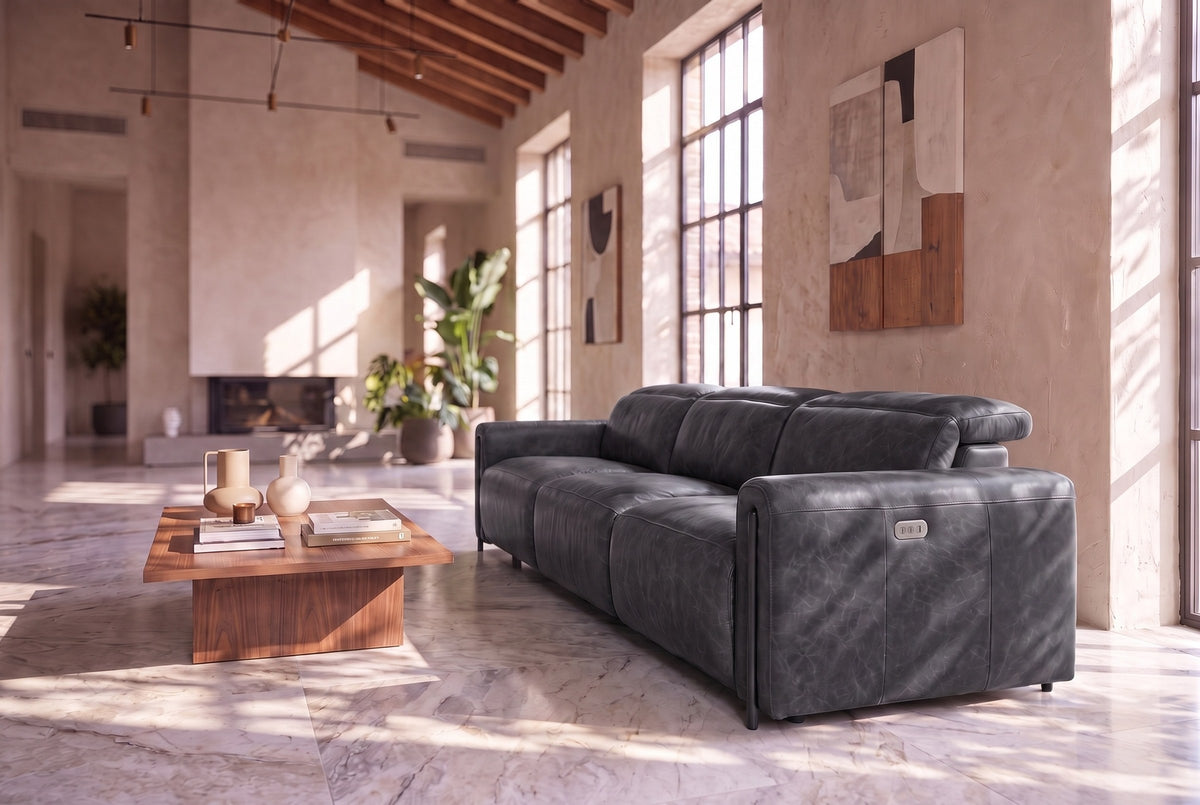 The Octavia 3 seat seen from its right end in a sunlit plaster room with a timber ceiling and a marble floor, the near headrest raised. Shown in Aged Slate, 3 seat.