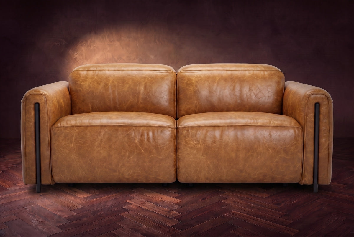 The Octavia loveseat in Antiqued Caramel distressed full leather on a dark herringbone floor, seen from the front, headrests down. Shown in Antiqued Caramel, Loveseat.