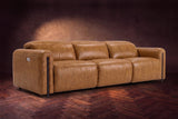 The Octavia 3 seat in Antiqued Caramel distressed full leather on a dark herringbone floor, headrests down and footrests closed. Shown in Antiqued Caramel, 3 seat.