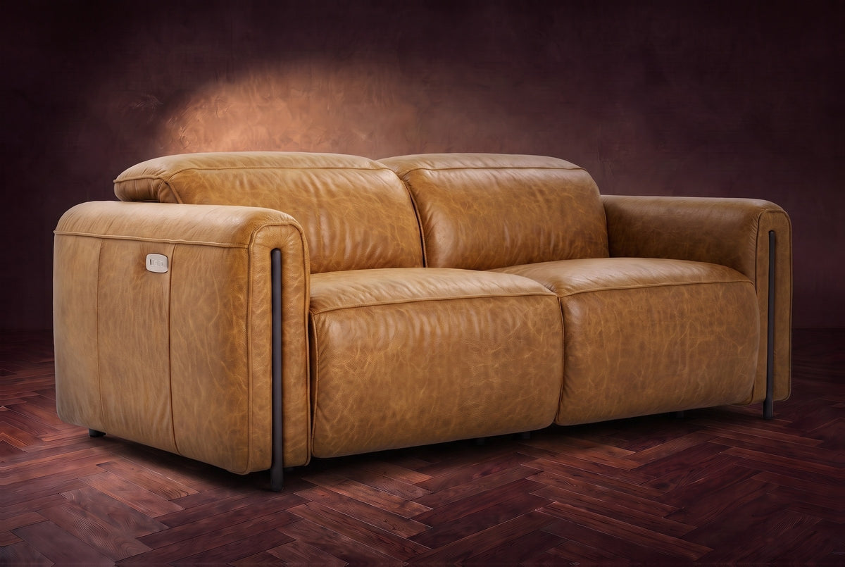 The Octavia loveseat in Antiqued Caramel distressed full leather on a dark herringbone floor, headrests down and footrests closed. Shown in Antiqued Caramel, Loveseat.