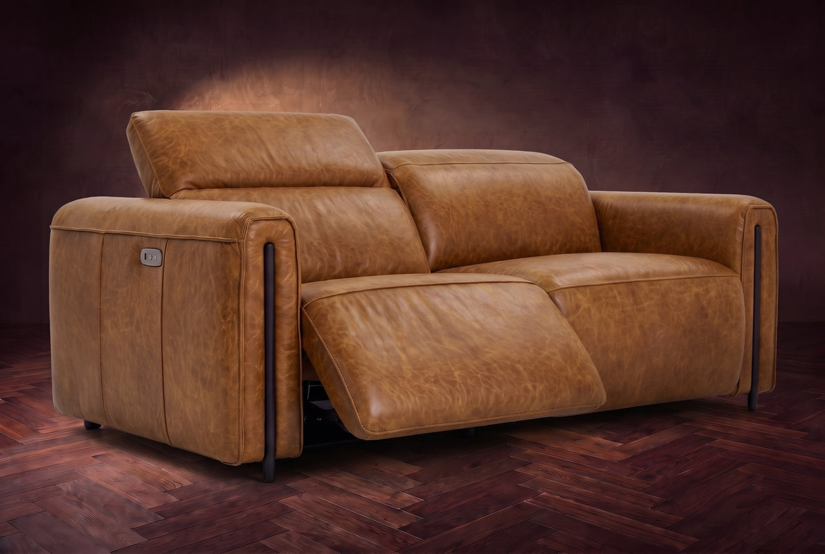 The Octavia loveseat in Antiqued Caramel distressed full leather on a dark herringbone floor, the left recliner open and its headrest raised. Shown in Antiqued Caramel, Loveseat.