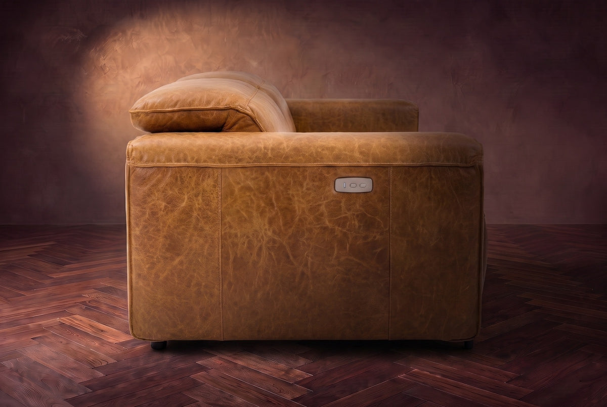 The Octavia loveseat in Antiqued Caramel distressed full leather on a dark herringbone floor, seen from the side, one headrest raised.