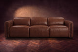 The Octavia 3 seat in Burnished Chestnut distressed full leather on a dark herringbone floor, seen from the front, headrests down. Shown in Burnished Chestnut, 3 seat.
