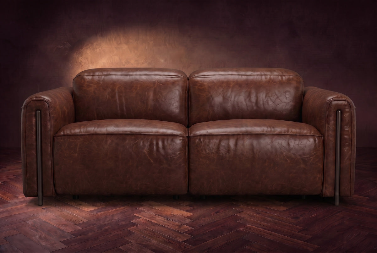 The Octavia loveseat in Burnished Chestnut distressed full leather on a dark herringbone floor, seen from the front, headrests down. Shown in Burnished Chestnut, Loveseat.