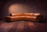 Octavia sectional in Tuscan Cognac on a walnut herringbone floor, low three-quarter view from further back, footrests closed, Left bumper.