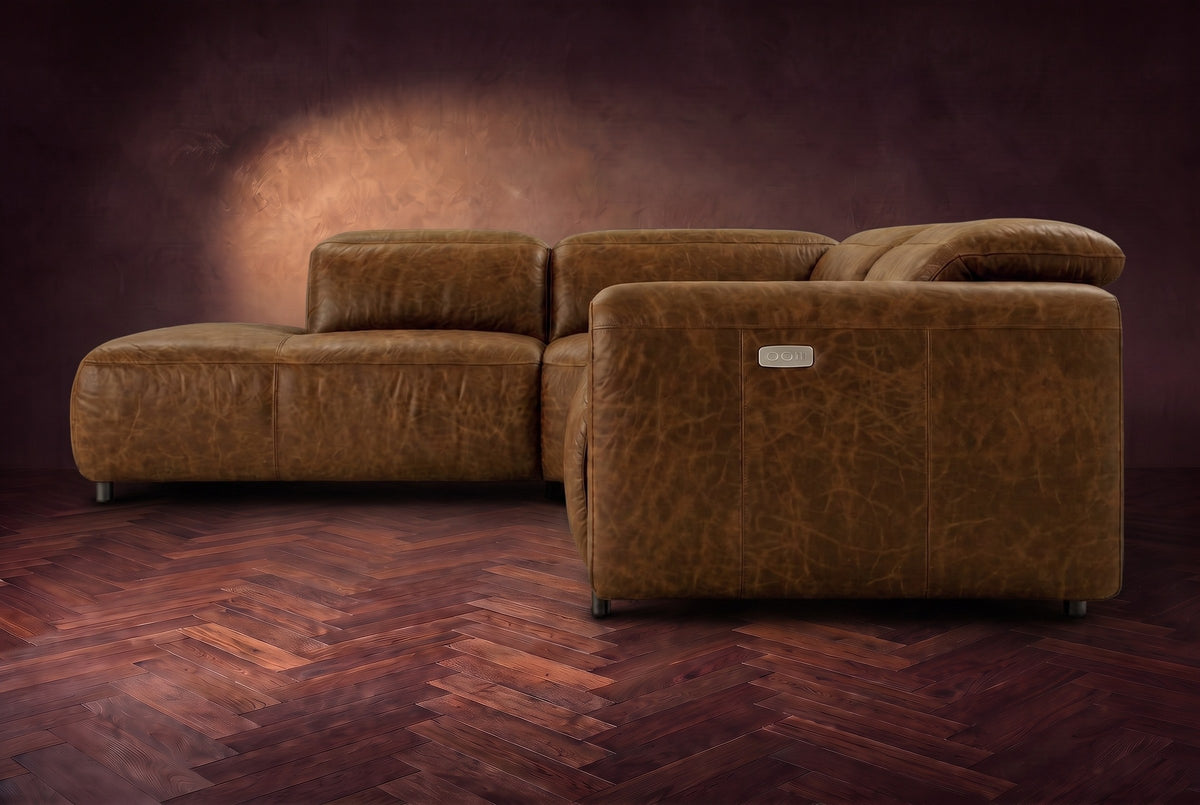 Octavia sectional in Weathered Saddle on a walnut herringbone floor, seen from the arm end, footrests closed, Left bumper.