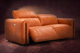 The Octavia loveseat in Tuscan Cognac distressed full leather on a dark herringbone floor, the left recliner open and its headrest raised. Shown in Tuscan Cognac, Loveseat.