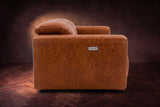 The Octavia loveseat in Tuscan Cognac distressed full leather on a dark herringbone floor, seen from the side, one headrest raised.