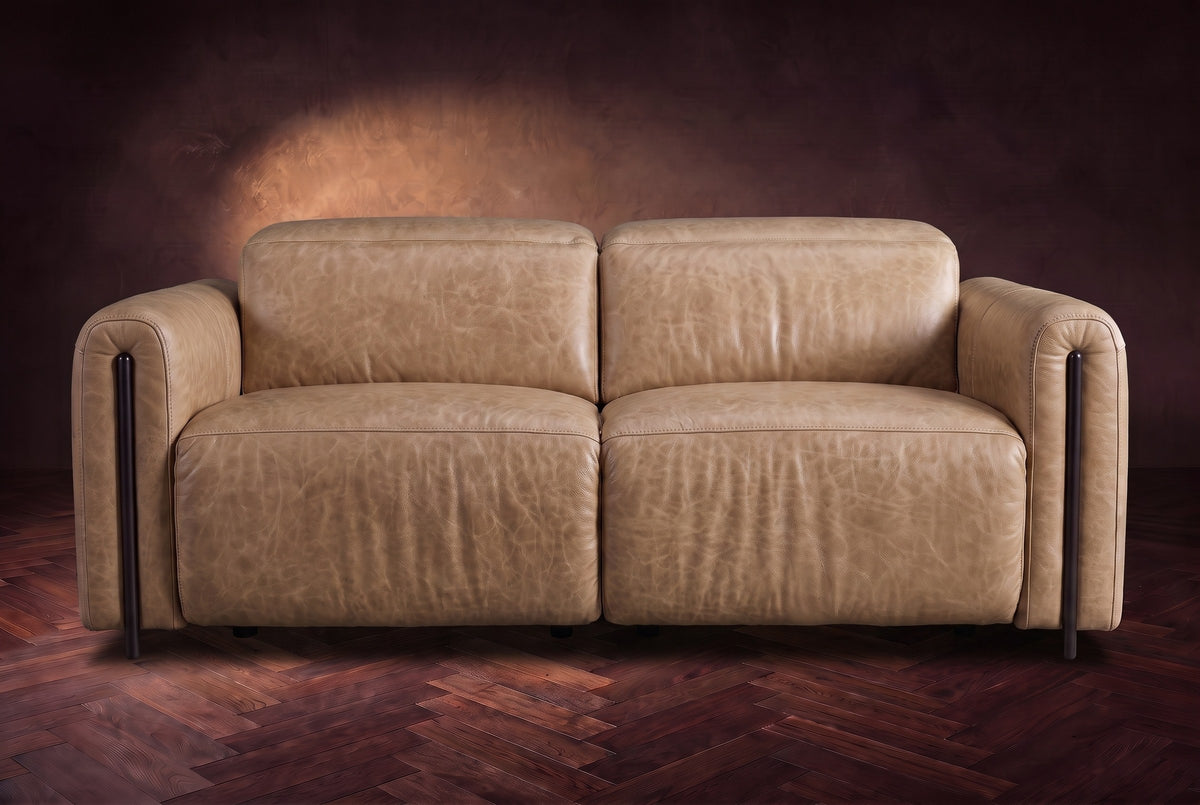 The Octavia loveseat in Washed Sand distressed full leather on a dark herringbone floor, seen from the front, headrests down. Shown in Washed Sand, Loveseat.
