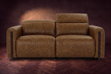 The Octavia loveseat in Weathered Saddle distressed full leather on a dark herringbone floor, seen from the front, the right headrest raised. Shown in Weathered Saddle, Loveseat.