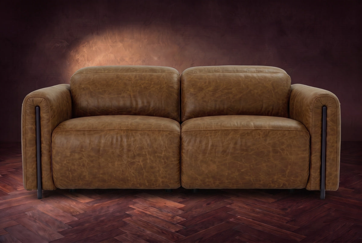 The Octavia loveseat in Weathered Saddle distressed full leather on a dark herringbone floor, seen from the front, headrests down. Shown in Weathered Saddle, Loveseat.