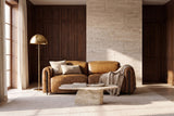 The Octavia loveseat against a travertine wall in a walnut-panelled room, cushions and a knit throw on it. Shown in Weathered Saddle, Loveseat.