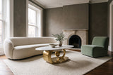 The Oriana coffee table on an ivory rug in a parlour with deep greige plaster walls, a marble fireplace, an ivory boucle sofa and a soft green velvet chair