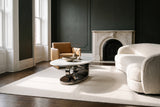 The Oriana coffee table in Gray on an ivory rug in a parlour with charcoal-green plaster walls, a white marble fireplace, an ivory boucle sofa and a camel leather chair