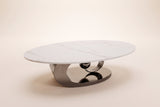 The Oriana coffee table in Gray seen from a low side angle, showing the slim stone edge and the gunmetal ring and sphere beneath it, on an off-white studio background
