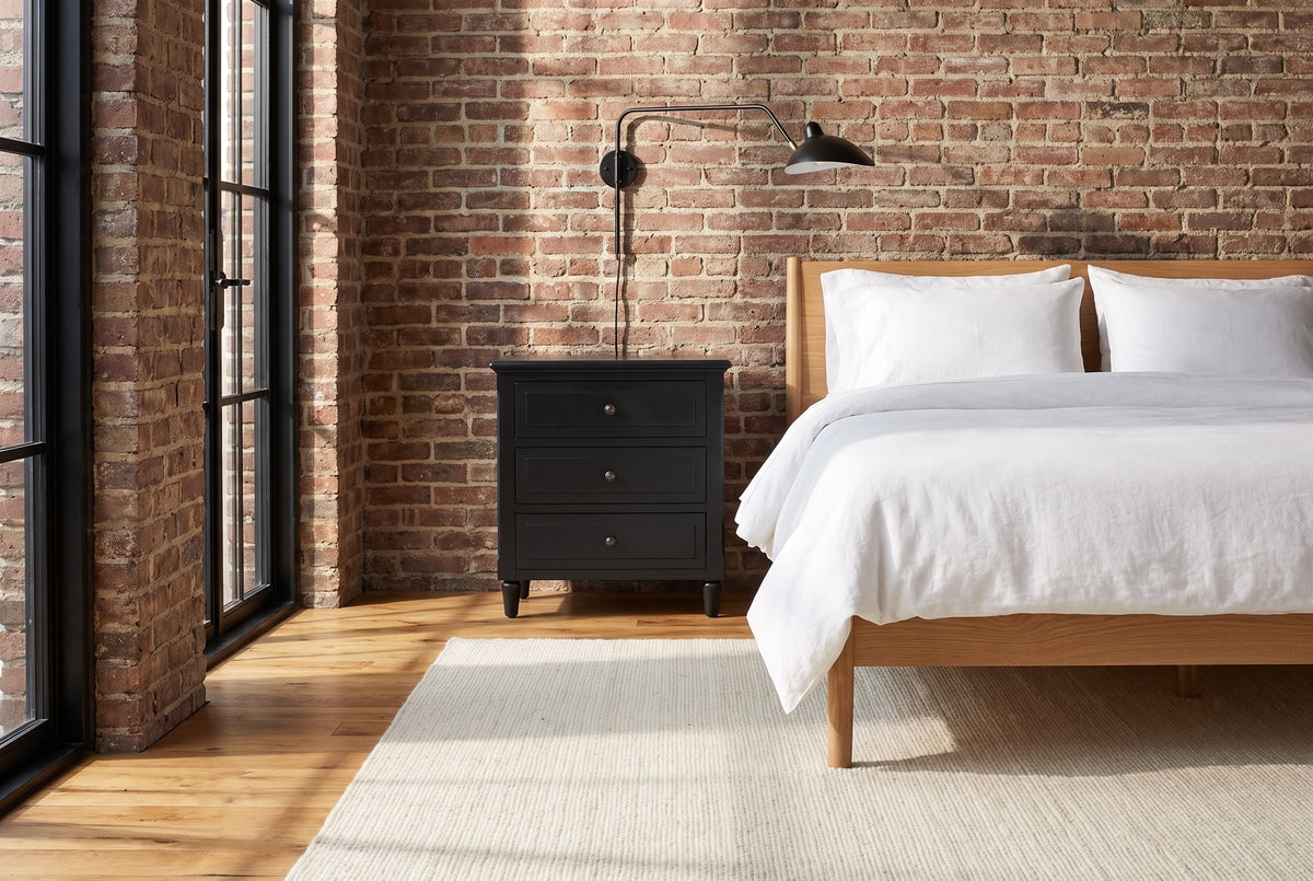 Ortona nightstand in Black against an old brick wall in a Montreal loft bedroom, a swing-arm lamp above it