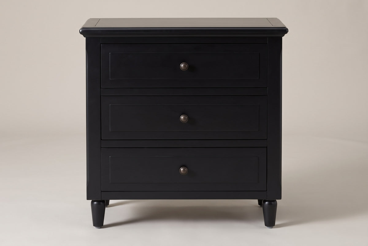 Ortona nightstand in Black, straight front view: moulded top, three drawers with round bronze-tone knobs, four turned legs