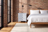 Ortona nightstand in White against an old brick wall in a Montreal loft bedroom, a swing-arm lamp above it