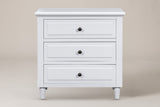 Ortona nightstand in White, straight front view: moulded top, three drawers with round bronze-tone knobs, four turned legs