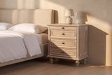 Osimo nightstand in Natural White beside a linen bed in late golden sun, its framed side panel in the light