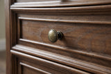Close-up of a framed walnut-brown drawer front with open ash grain and a round antique-brass-tone knob