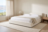 Otranto bed made up with white linen in a bright bedroom with pale oak nightstands and a window onto a lake and vineyards