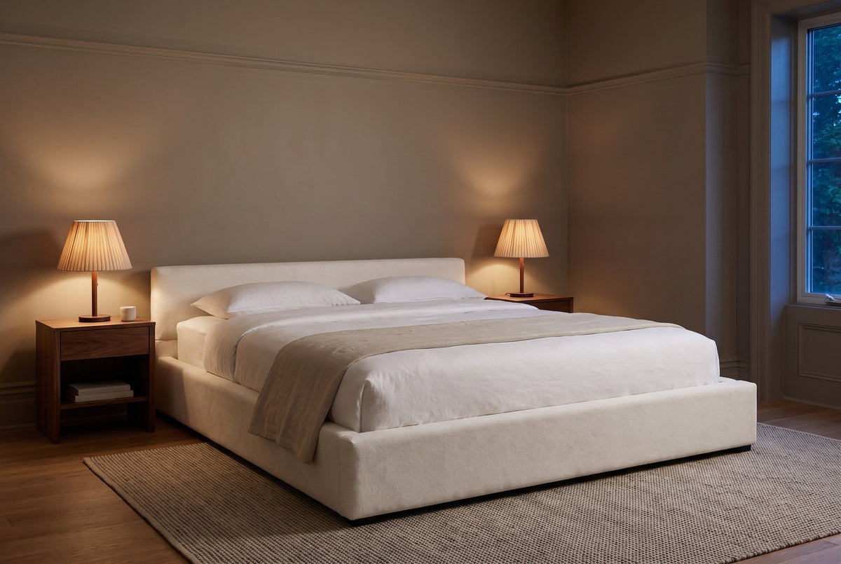 Otranto bed in a taupe bedroom at dusk, pleated lamps lit on two walnut nightstands