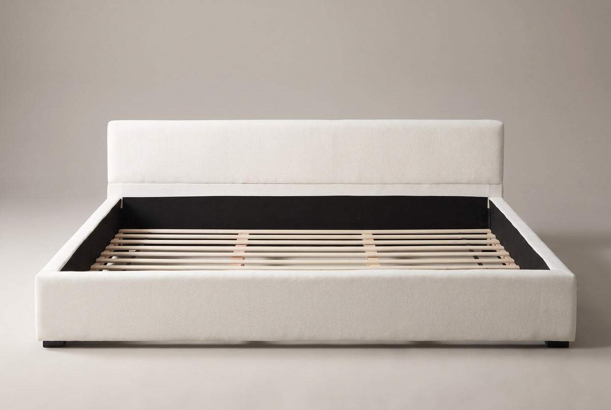 Otranto bed, straight front view: a low padded headboard and a wide upholstered rim on black block feet