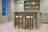 Two Otricoli bar stools in Ivory at a sage-green panelled home bar with a marble top and brass pendant lamps in a Toronto tow