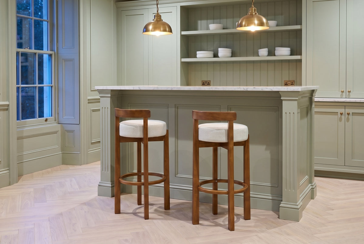 Two Otricoli bar stools in Ivory at a sage-green panelled home bar with a marble top and brass pendant lamps in a Toronto tow