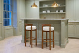 Two Otricoli bar stools at a sage-green panelled home bar with a marble top and brass pendant lamps in a Toronto townhouse