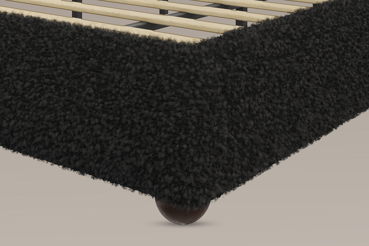 Close-up of the black teddy foot corner of the rail, the pale slats inside it and a dark ball foot