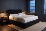 Padula bed in black in a slate-blue bedroom at dusk, brass lamps lit and harbour lights in the window