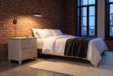 Palestrina nightstand in Beige beside a bed with white linen in a brick-walled Montreal loft at dusk