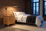 Palestrina nightstand in Natural beside a bed with white linen in a brick-walled Montreal loft at dusk
