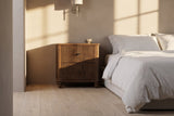 Palestrina nightstand in Walnut beside a low bed in a plaster bedroom at golden hour