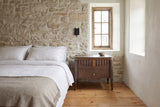 Pavia nightstand in Brown beside a bed against a limestone wall in an old Quebec City house