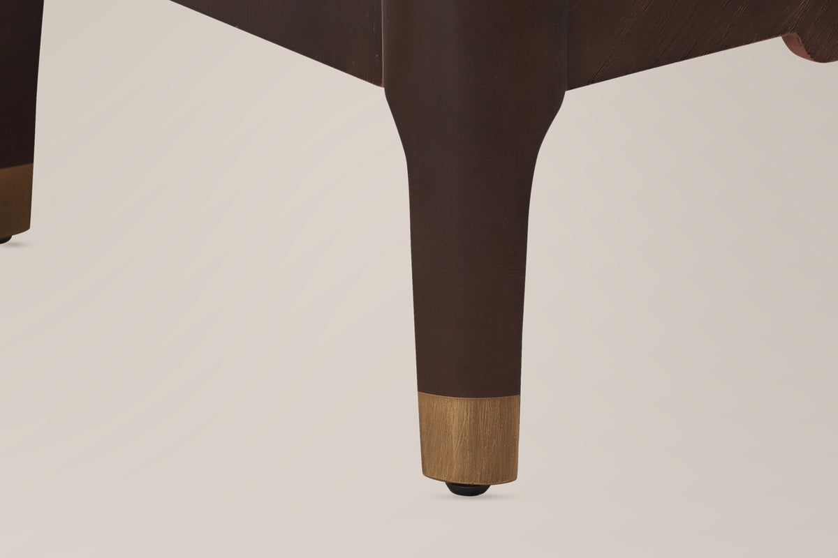 Close-up of a Pavia corner post in Dark Brown running into a tapered leg with a gold-tone cap and a floor glide