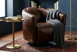 Percival brown bi-cast leather club chair with a grey throw beside a brass floor lamp and bookshelf