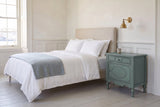 Perugia nightstand in Aged Blue beside a bed with white linen in a bright Halifax bedroom with white wainscot and a brass sco