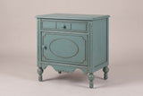 Perugia oval-panel nightstand in Aged Blue, three-quarter view on a warm grey studio backdrop