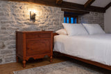 Perugia nightstand against a fieldstone wall in a Quebec City bedroom at dusk, an iron sconce lit above it