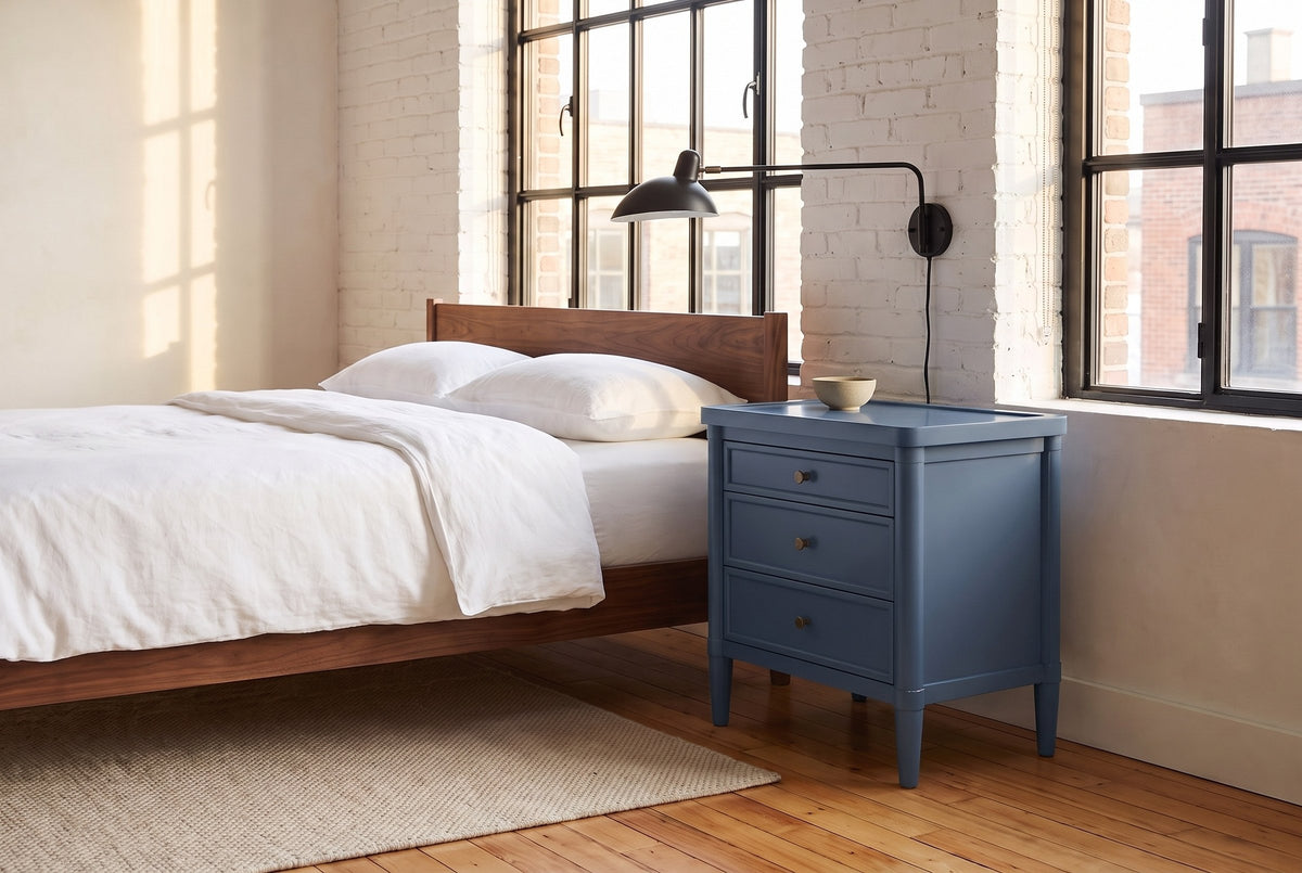 Pescara nightstand in Navy Blue beside a walnut bed in a whitewashed brick Montreal loft, a black swing-arm lamp above it