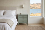 Pescara nightstand in Sage Green beside a bed in a Kelowna lake house bedroom with a view of the lake and dry hills
