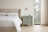 Pescara nightstand in Sage Green beside a bed with white linen in a plaster Vancouver bedroom with a misty cedar view