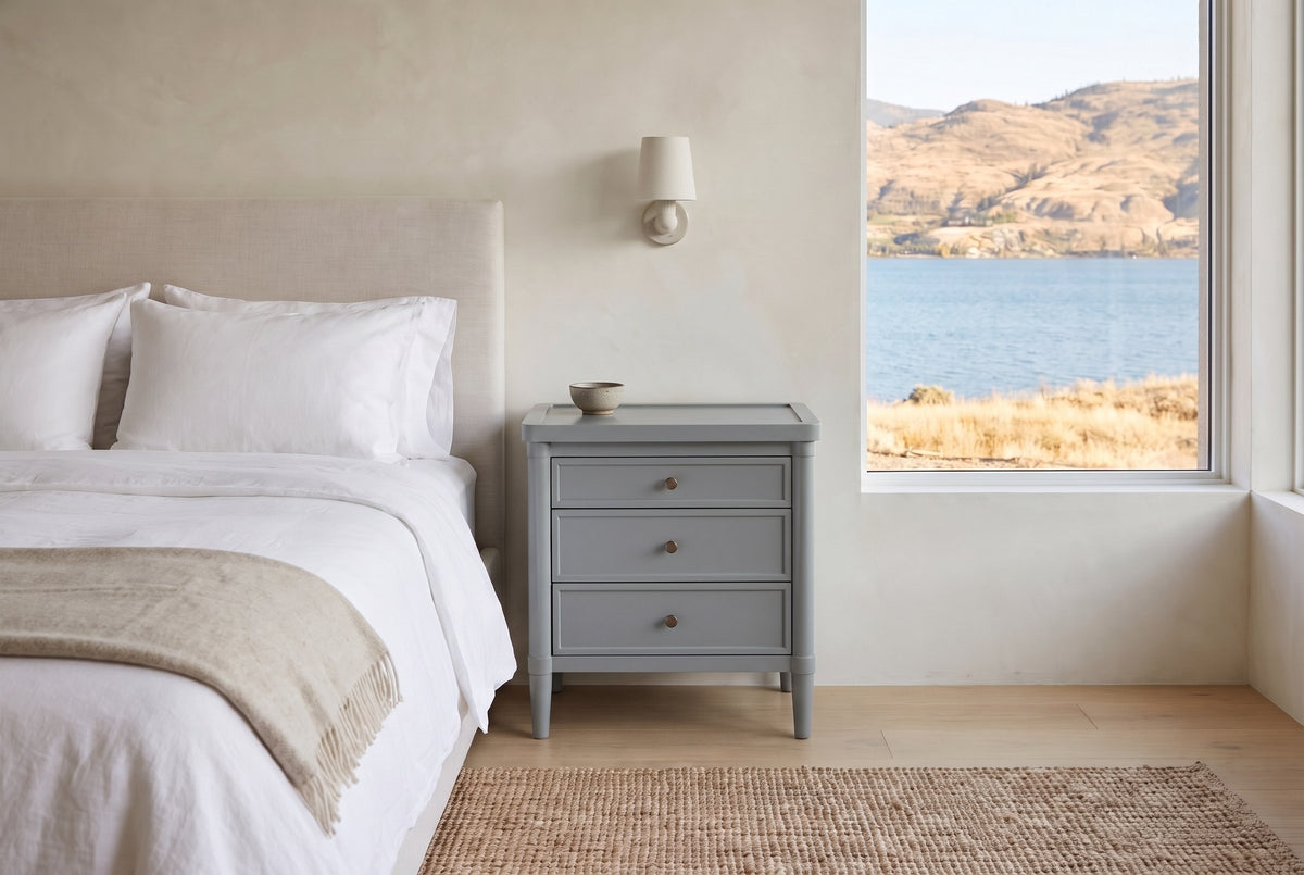 Pescara nightstand in Slate Gray beside a bed in a Kelowna lake house bedroom with a view of the lake and dry hills