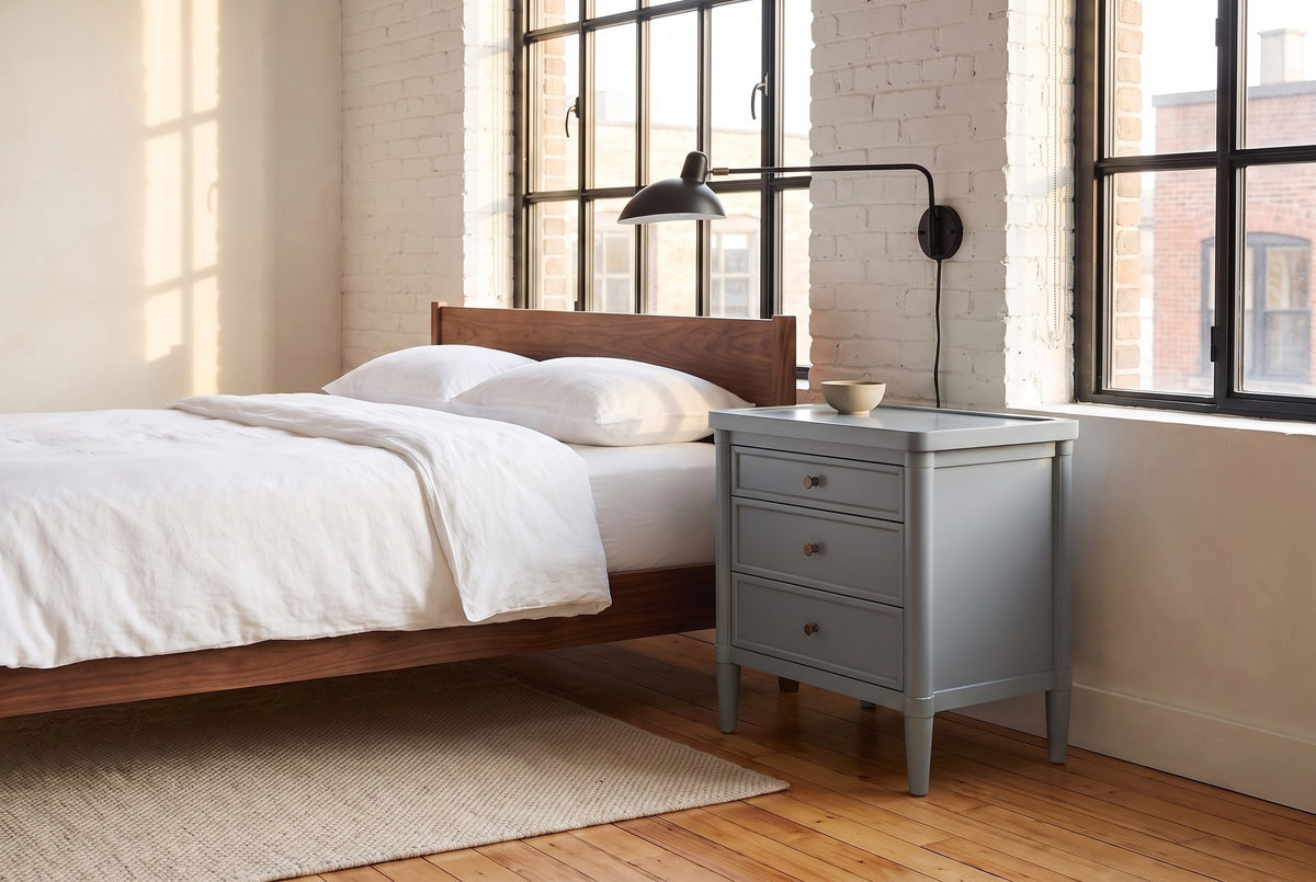 Pescara nightstand in Slate Gray beside a walnut bed in a whitewashed brick Montreal loft, a black swing-arm lamp above it