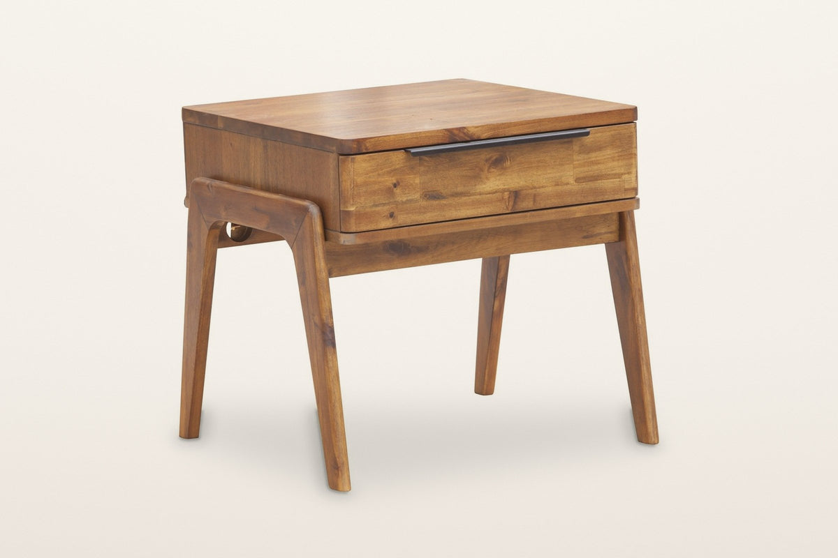Pescasseroli end table in Brown acacia, three-quarter view on a warm white studio backdrop: one drawer with a black bar pull under the top, bent-wood side frames on four splayed legs