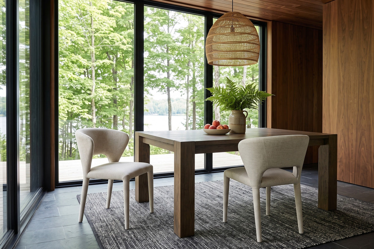 Two Petralia dining chairs in Beige tweed at the corner of a square smoked-oak table in a Haliburton forest house