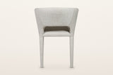 Back of the Petralia dining chair in Beige tweed on a warm white studio backdrop: a smooth wrapped shell with a low slot abov